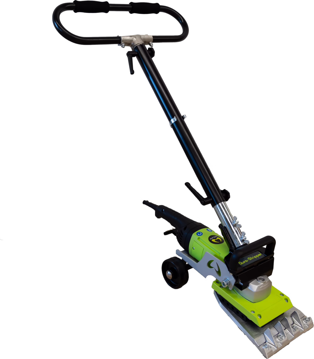 A powered floor stripping tool photographed on a white background. The device has a long black adjustable tubular handle with foam grips and a height-adjustment clamp, connected to a green and black motor housing mounted on a silver metal chassis with small transport wheels. At the working end there is a rectangular serrated metal scraping plate fixed with bolts and a black protective handguard bearing a printed label; the assembly shows visible fasteners, a pivot/angle joint and a lever for locking the head position. The tool appears designed for removing floor coverings, adhesive residues or tile adhesive in renovation and construction work; materials include painted metal, cast components and plastic housings, and the overall appearance is compact, robust and purpose-built for heavy-duty scraping tasks.